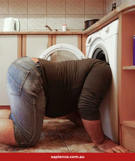 man kneeling on ground with his head in a front loader washing machine door