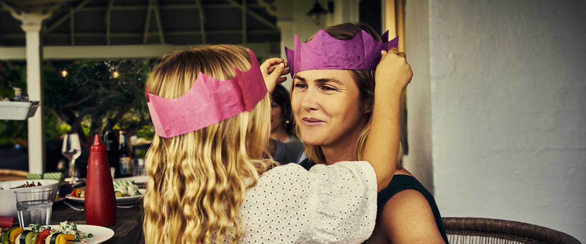 young girl and mother both wearing a pink party paper hat