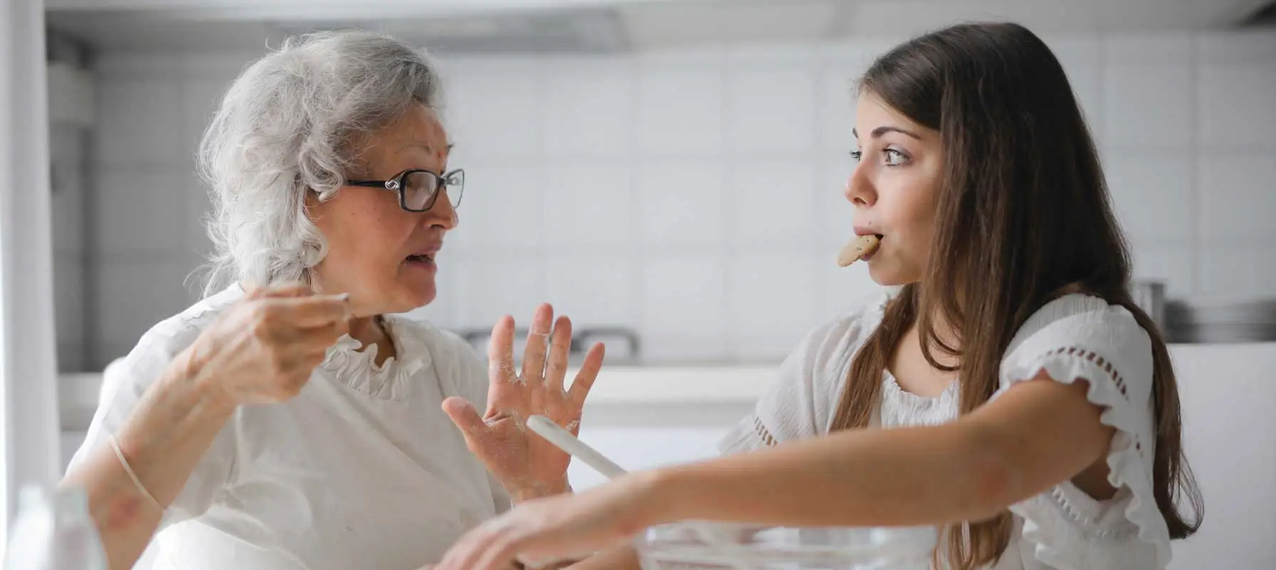 grandmother cooking with teen granddaughter who is still eating cookies