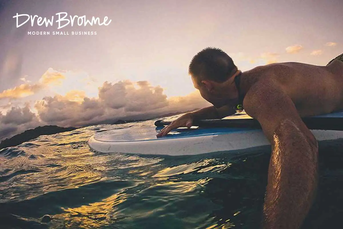 A close up image of a surfer on a bold at sunrise looking out to fluffy white clouds