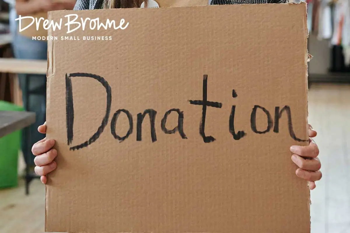 A person holding a large cardboard sign with the word donation displaying written in black crayon