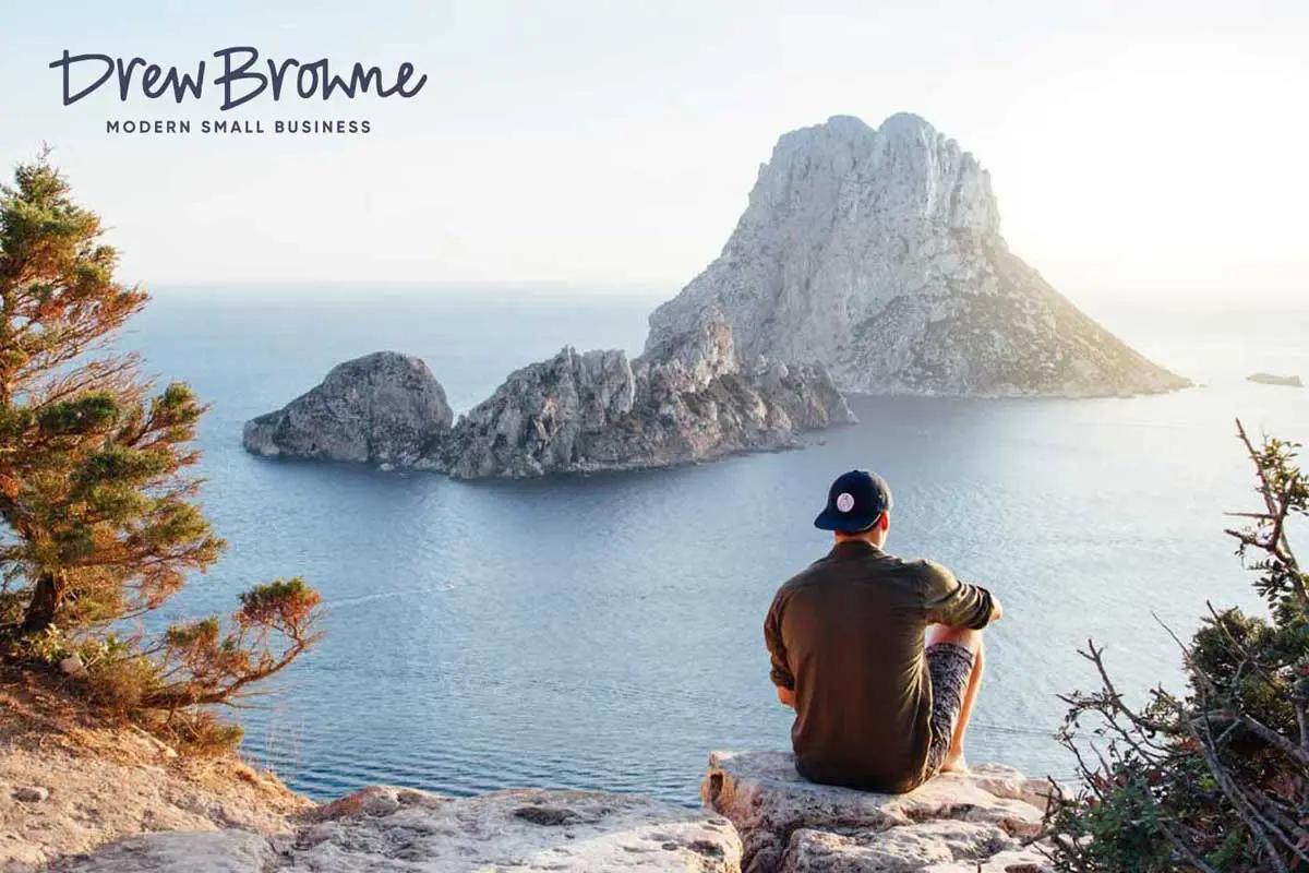 young man sitting on rock looking at the ocean while wearing a cap